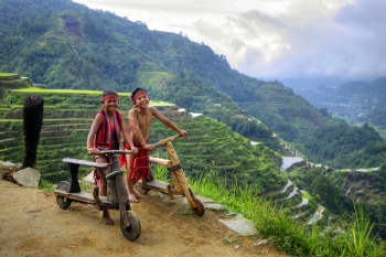 Photo of two Indigenous boys from Northern Luzon wearing their "wanoh" or traditional clothing while riding a wooden bike