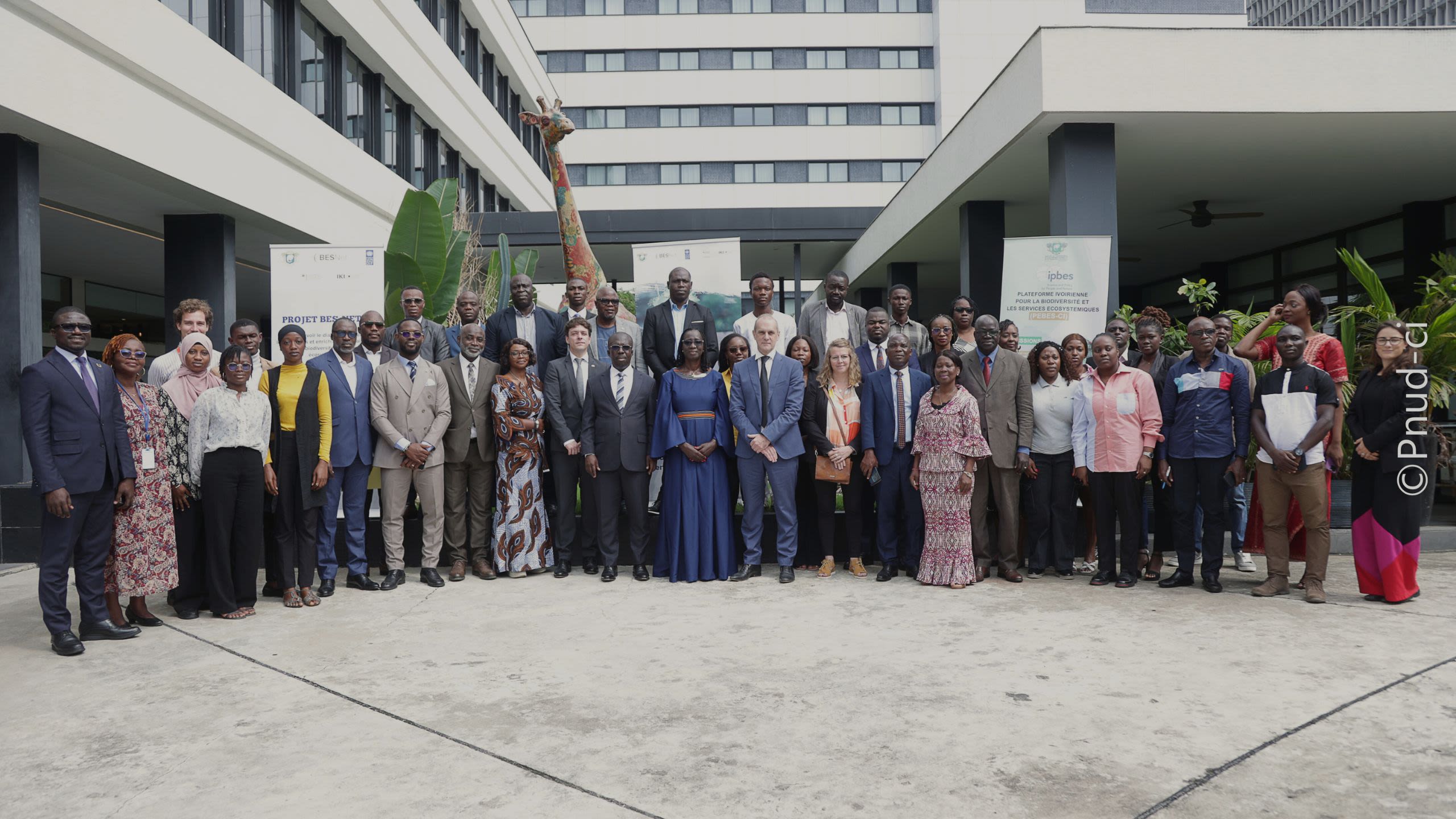 A photograph of a lush, green forest pathway with two people walking along a muddy dirt trail.