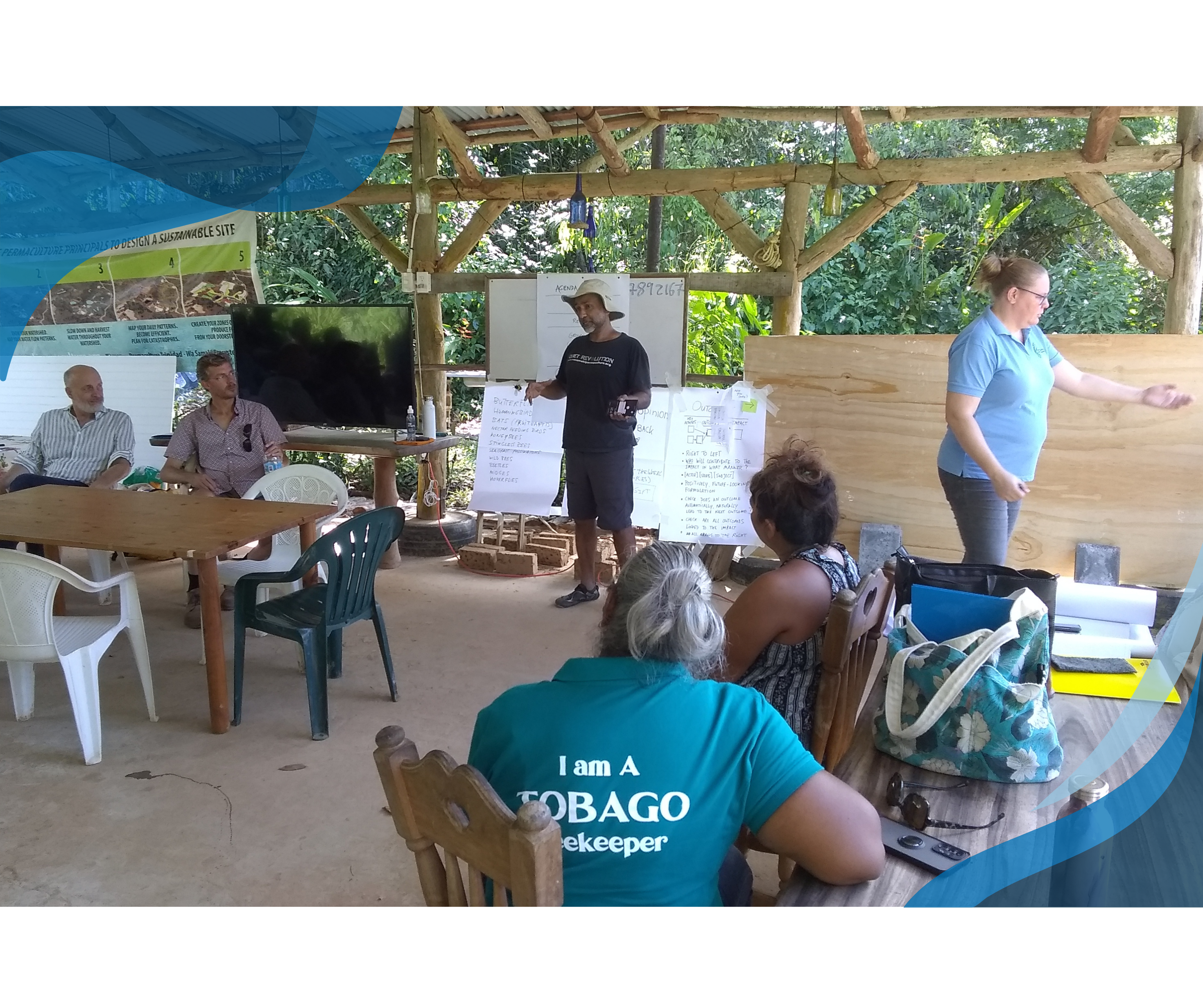 A group of people engaged in a workshop or training session in an open-air structure, with some participants seated and others standing and presenting.