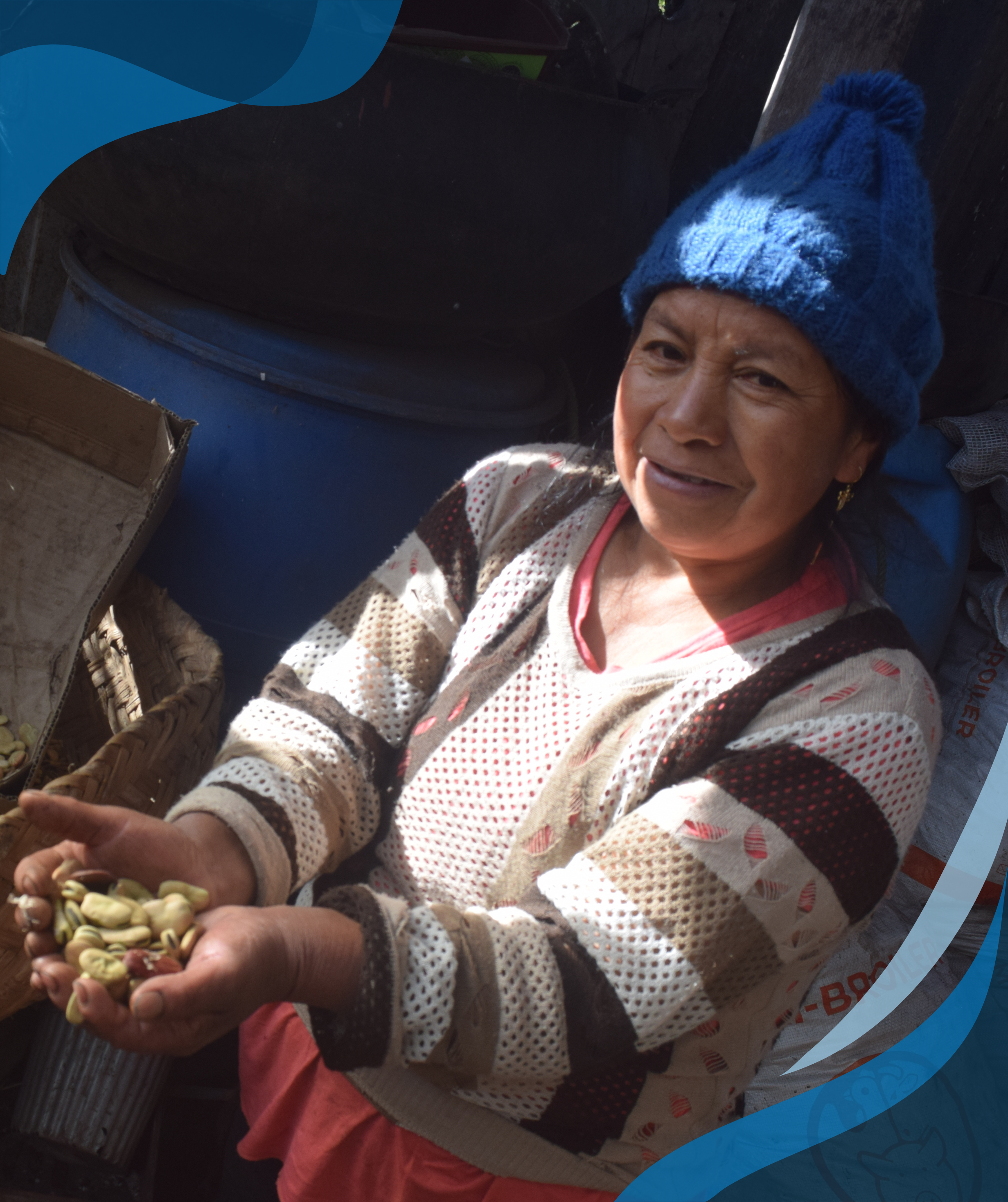 A woman with a blue knit hat holds a handful of seeds while standing next to a large basket filled with more seeds, surrounded by sacks and other containers.