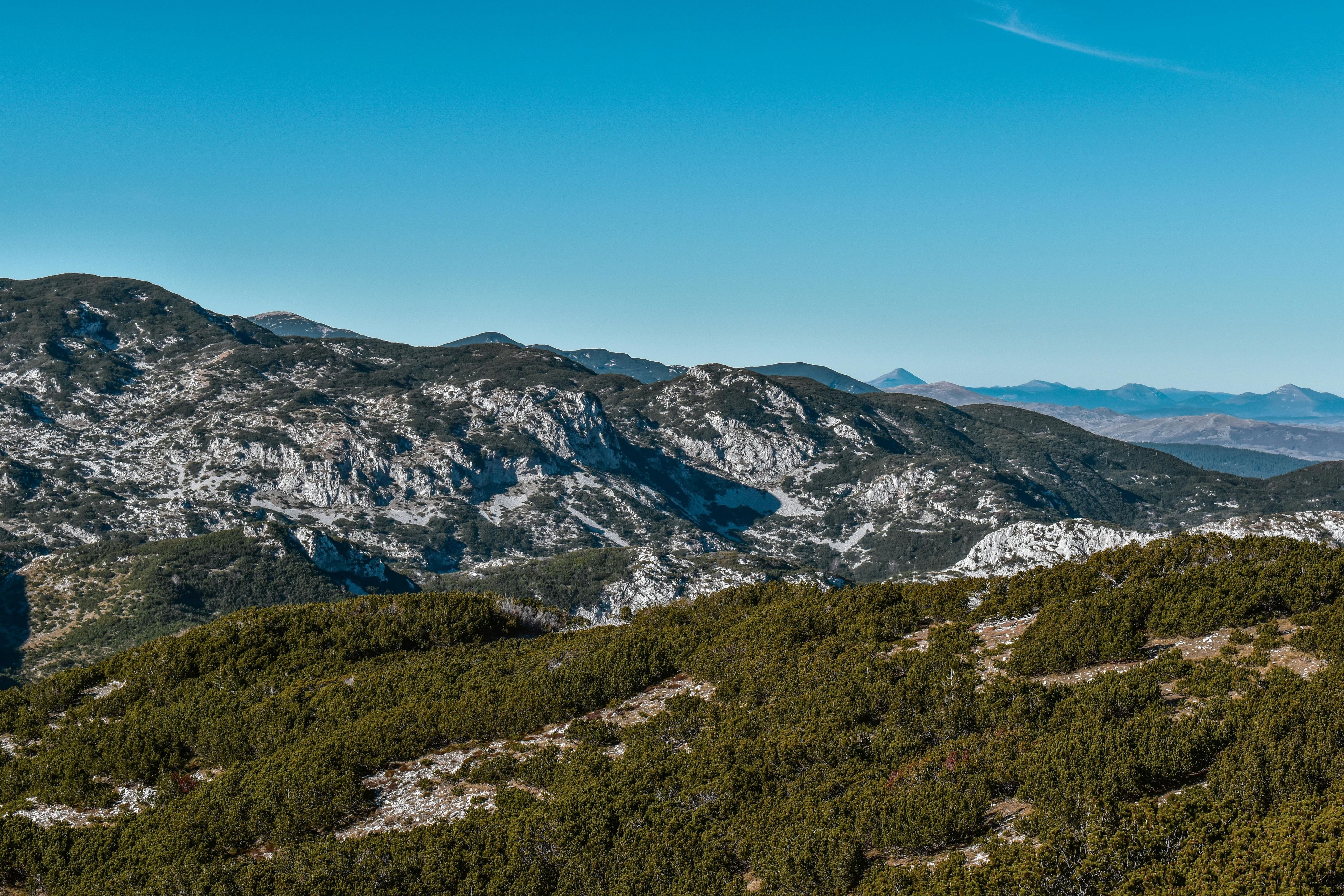 Mountain landscape with rugged rocky slopes and patches of green vegetation under a clear blue sky.