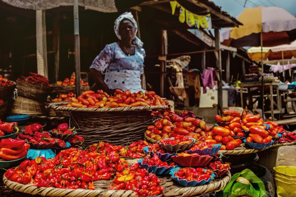 Photo of a market with a woman selling vegetables.